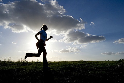 Running woman as a silhouette in front of a sky in back light