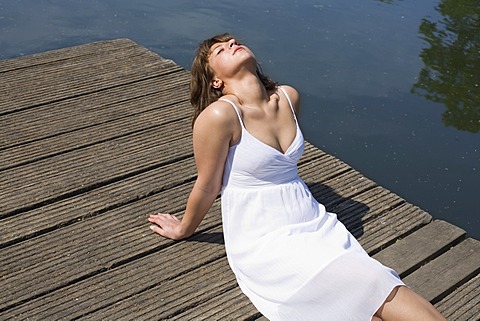 Woman in a white dress sitting on a boardwalk enjoying the sun