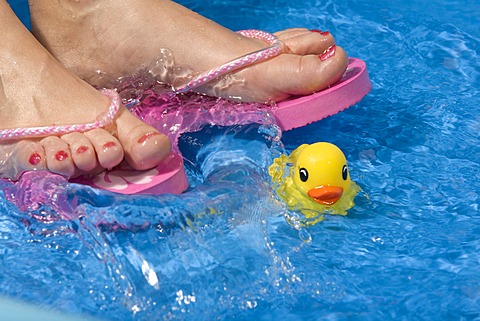 Feet wearing flip-flops in a paddling pool with a rubber duck