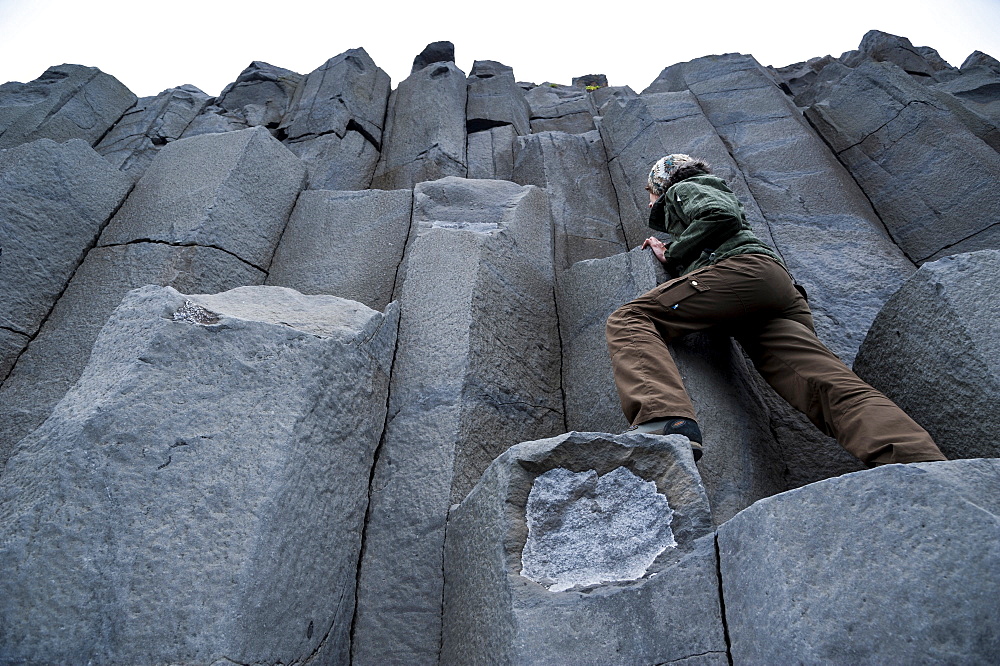 Woman climbing on basalt columns, Halsanefshellir cave, Reynisfjara beach at Vik i Myrdal, South Coast, Iceland, Europe