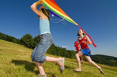 Two girls running with a kite in a meadow in the Black Forest, Baden-Wuerttemburg, Germany, Europe