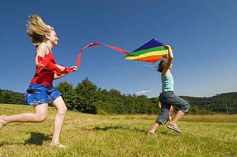 Two girls running with a kite in a meadow in the Black Forest, Baden-Wuerttemburg, Germany, Europe