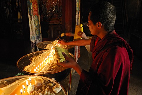 Pilgrim and Tibetan monks refilling the brass bow with yak butter, Samye Monastery, Tibet, China, Asia