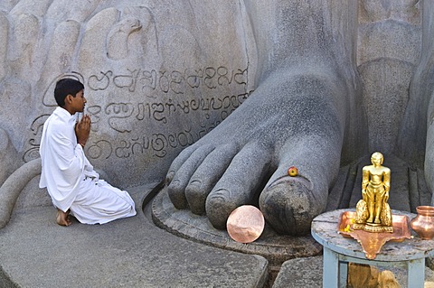 Jain pilgrim is praying at the feet of the gigantic statue of Gomateshwara in Sravanabelagola, Karnataka, India, Asia