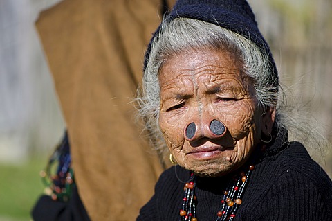 Old Apatani woman with the traditional noseplugs and tattoos, in front of her house, Dutta village, Arunachal Pradesh, India, Asia