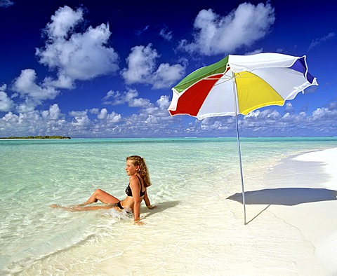 Young woman laying in shallow water, umbrella, paradise beach, Maldives, Indian Ocean