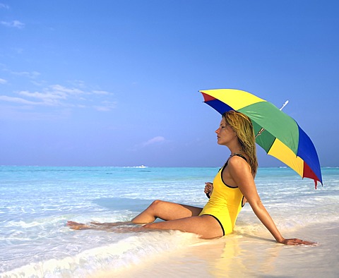 Young woman sitting in shallow water with sun umbrella, Maldives, Indian Ocean