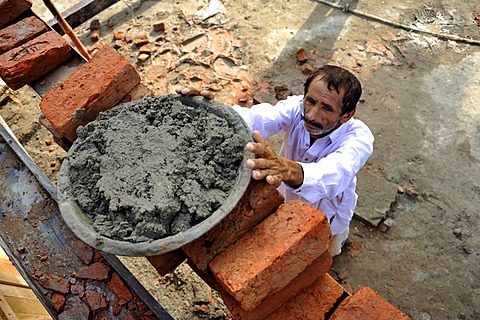 Man lifting pan with cement onto a scaffold, construction of brick houses for families whose houses were destroyed during the flood catastrophe of 2010, Lashari Wala village near Muzaffaragarh, Punjab, Pakistan, Asia