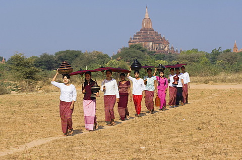 Young Burmese women with a parasol crossing a field near the Sulamani Pagoda, Bagan, Myanmar