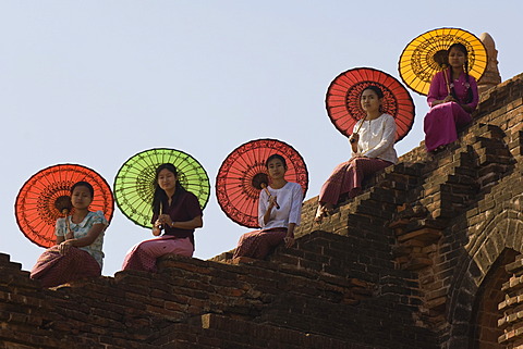 Young Burmese women with coloured parasols sitting on a temple wall, Bagan, Myanmar