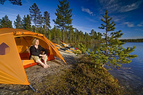 Woman sitting in front of a tent at a lakeside, looking into the distance, Femundsmarka National Park, Femundsmark, Norway