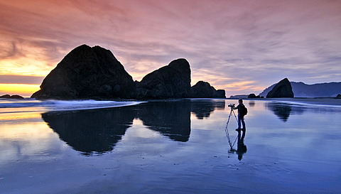 Camera woman with a film camera and tripod filming a sunset at Meyers Creek Beach, Pistol River State Park, Oregon coast, Oregon, USA, North America