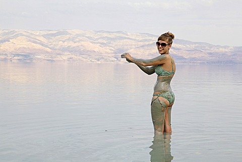 Young woman rubbing skin-soothing mud on herself, Dead Sea, West Bank, Israel, Middle East