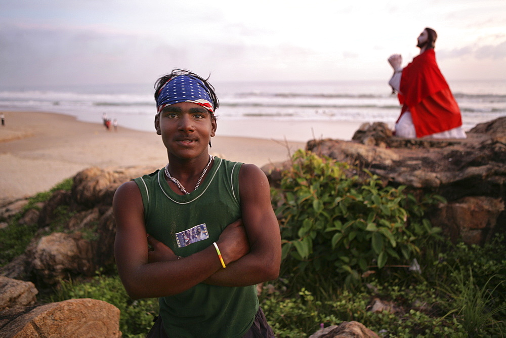 |IND, India, Kerala, Trivandrum : Malabar coast, south of Trivandrum, teenager at the beach. Jesus statue at the beach, near a little pilgrimage chapel. |