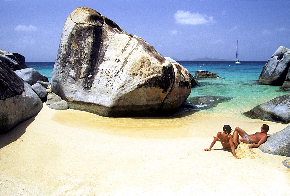 Sunbathing couple, sailboat in the distance, "The Baths, " Virgin Gorda Island, British Virgin Islands, Lesser Antilles, Caribbean