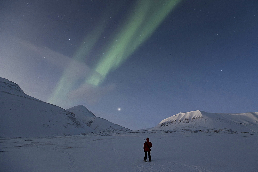 Person carrying a rifle is admiring the Northern lights and the starry sky, Spitsbergen, Svalbard, Norway, Europe