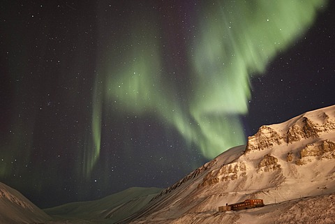 Strong green Northern Lights, Aurora Borealis, above a historic building lit by the lights of the town of Longyearbyen, Longyearbreen Glacier at back, Spitsbergen, Svalbard, Norway, Europe