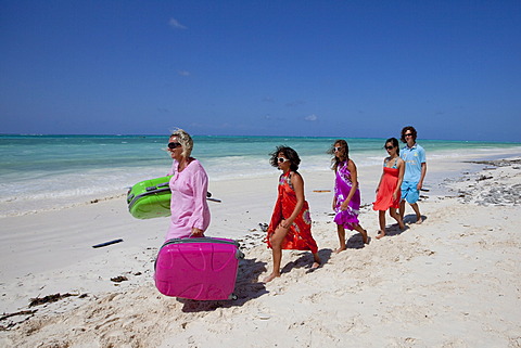 Mother on holiday carrying the suitcases for her family on her own on the beach