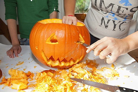 Two girls, about 14 years, carving a face into a Halloween pumpkin