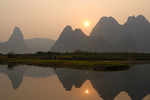 Karst cliffs and rice fields in the evening sun are reflected at harvest time in the Yulong River in the rocky karst landscape near Yangshuo, Guilin, Guangxi, China, Asia