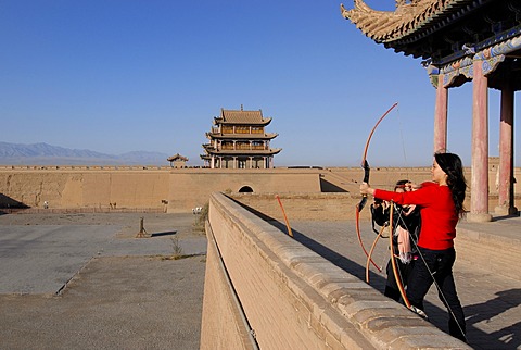 Chinese woman using a bow and arrow at the Jiayuguan Fortress with two gatehouses at the western end of the Great Wall of China, Silk Road, Gansu, China, Asia