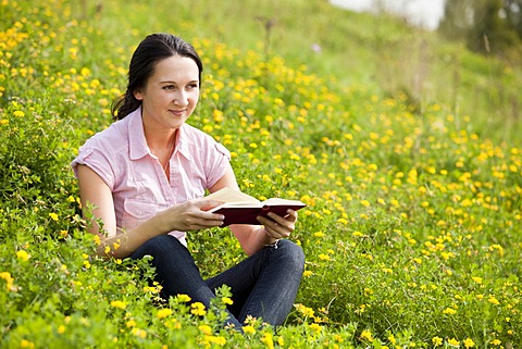 Young woman sitting on a meadow, reading a book