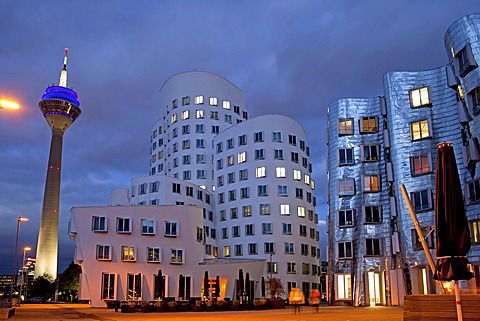 A building by American architect Frank O. Gehry and the Rheinturm tower at night, Neuer Zollhof building complex, Medienhafen district, Duesseldorf, North Rhine-Westphalia, Germany, Europe