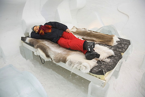 Tourist lying on a bed in a hotel room of the ice hotel in Jukkasjaervi, Lappland, Northern Sweden