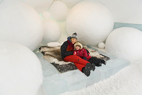 Woman and a 4-year-old girl sitting on a bed in a hotel room of the ice hotel in Jukkasjaervi, Lappland, Northern Sweden