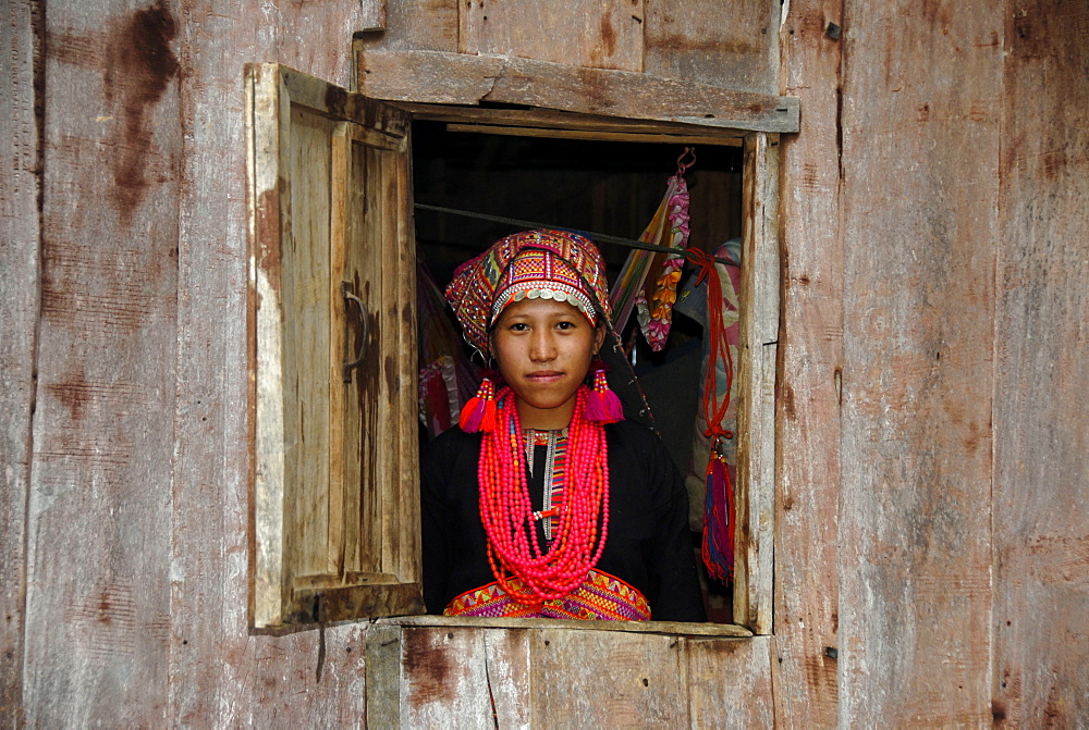 Young woman of the Akha Pala tribe looking out of a window dressed in a colourful head-dress and a red necklace, Ban Saenkham Tai, Phongsali Province, Laos, South East Asia