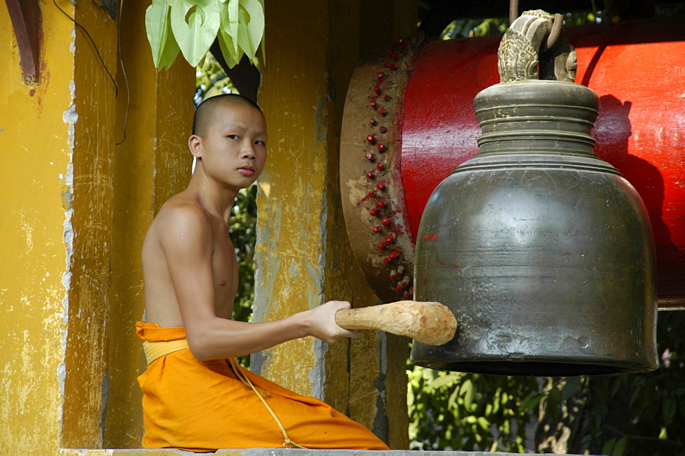 Young buddhist monk ringing the bell, Wat Sirimungkhun, Luang Prabang, Laos, Southeast Asia