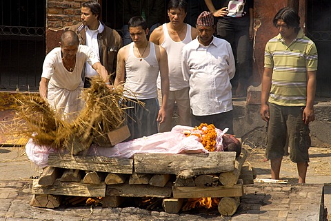 Traditional funeral, people standing around a body on a pyre, while an untouchable priest of the lowest caste spreads wet reed over the body, Pashupatinath, Nepal, Asia