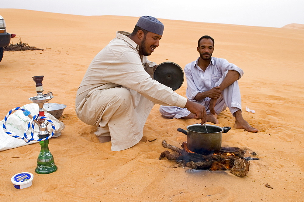 Libyan beduins sitting in the sand cooking their meal, Libya