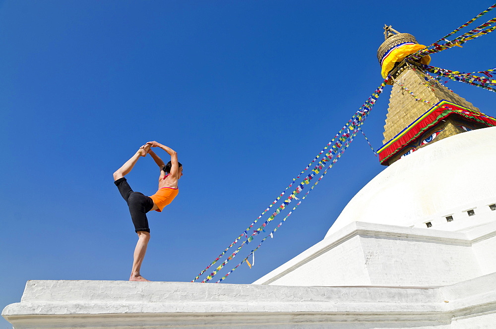 Young woman practicing yoga at Boudnanath stupa, showing the Natarajasana pose, or Lord Shiva's pose, Kathmandu Valley, Kathmandu, Kathmandu District, Bagmati Zone, Nepal, Asia