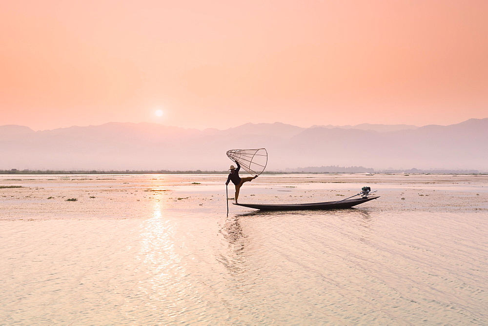 Inle lake fisherman standing on a longtail boat in the distinctive leg rowing stance used by the Intha people, Inle lake, Myanmar, Asia