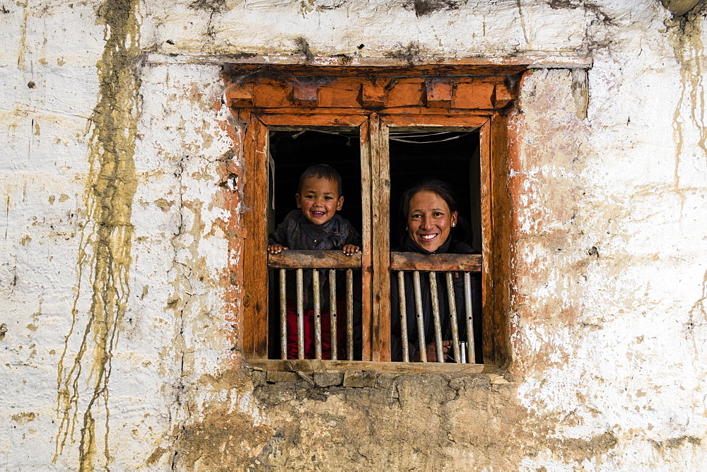 Young woman and son looking out of farmhouse window, Purang, Mustang District, Nepal, Asia