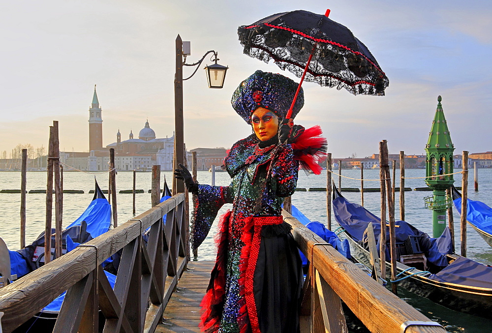 Female disguised with Venetian mask on walkway at the lagoon, behind island of San Giorgio, carnival in Venice, Italy, Europe