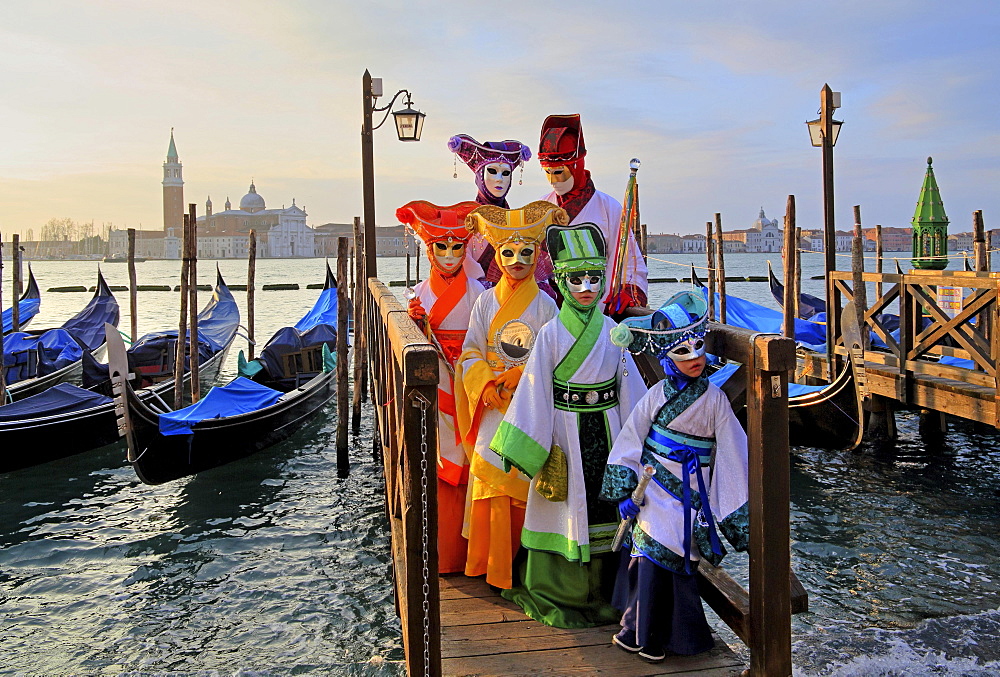 Disguised persons with Venetian masks on walkway at the lagoon, behind island of San Giorgio, carnival in Venice, Italy, Europe