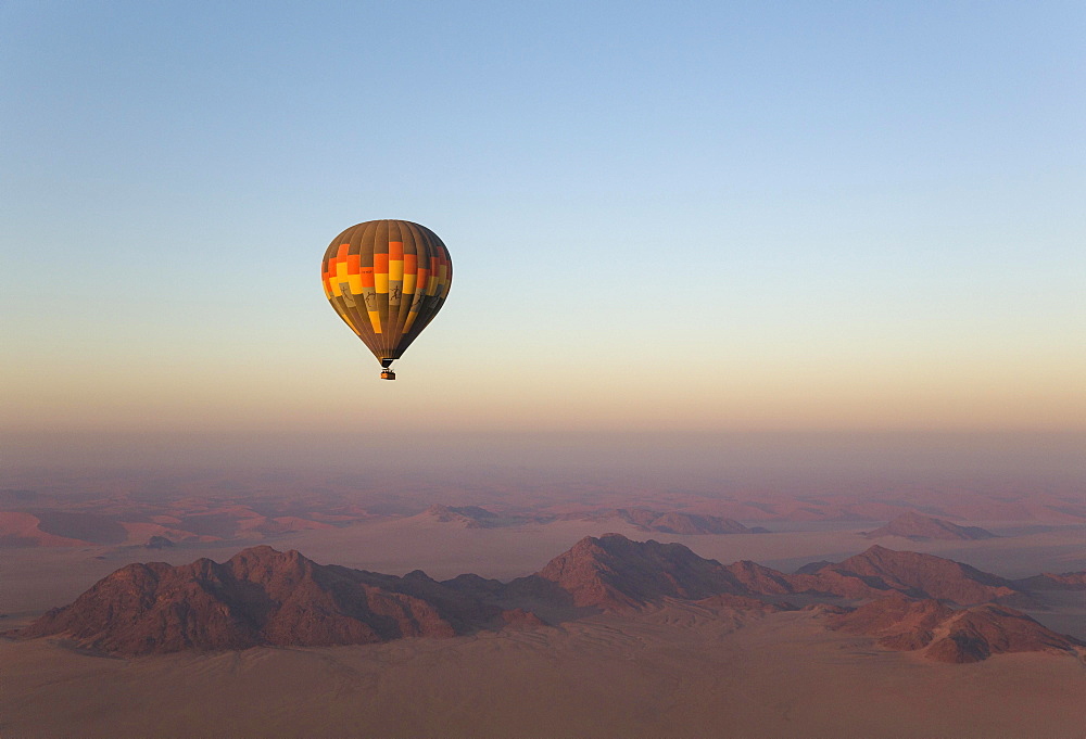 Hot-air balloon above an arid plain and isolated mountain ridges, at dawn, Namib Desert, aerial view from a second balloon, NamibRand Nature Reserve, Namibia, Africa