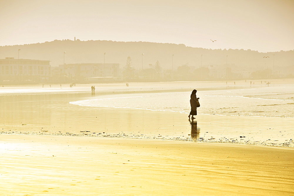 Rambler with a headscarf on the beach, silhouette in the morning light, Plage Tagharte, Essaouira, Morocco, Africa