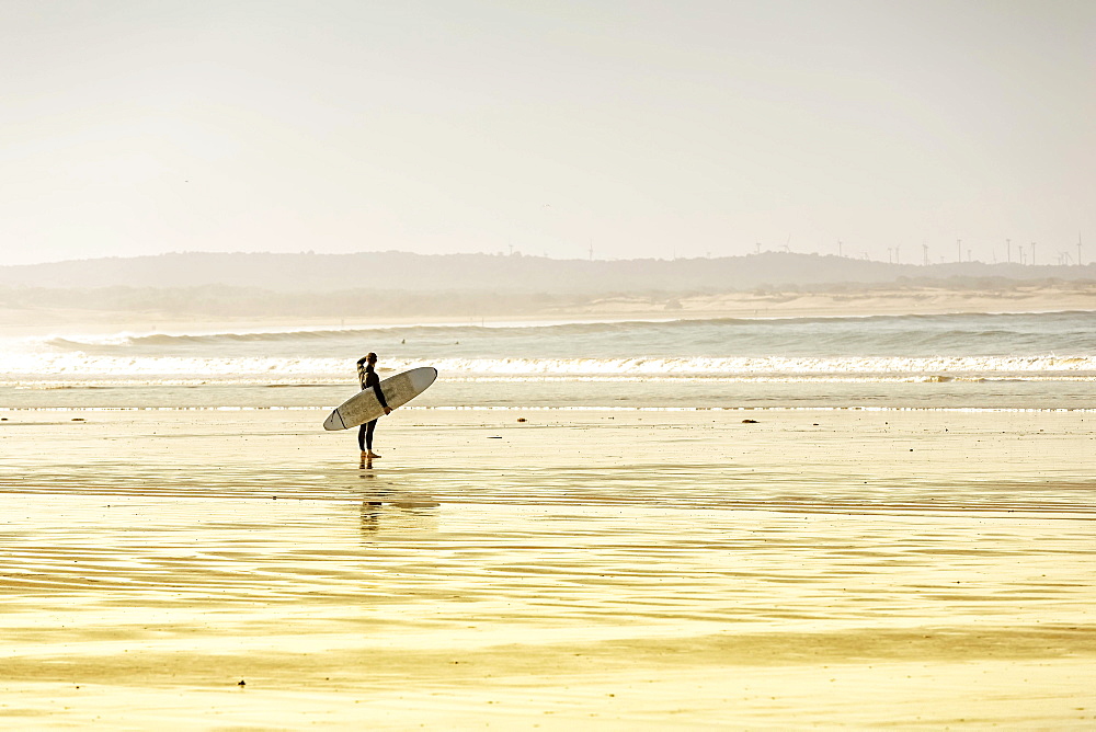 Surfer standing on the beach, watching the surf, Plage Tagharte, Essaouira, Morocco, Africa