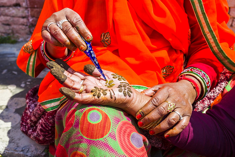 An indian woman is painting a hand with henna, in front of Badrinath Temple, one of the Dschar Dham destinations, Badrinath, Uttarakhand, India, Asia