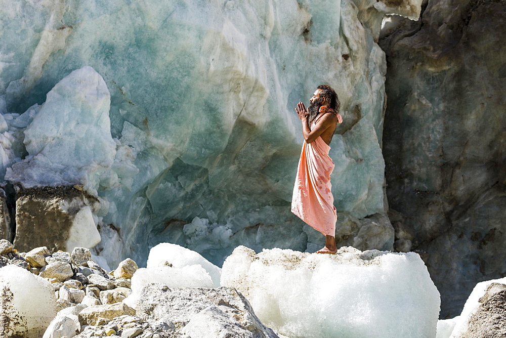 A Sadhu, holy man, is standing and praying on a block of ice at Gaumukh, the main source of the holy river Ganges, Gangotri, Uttarakhand, India, Asia