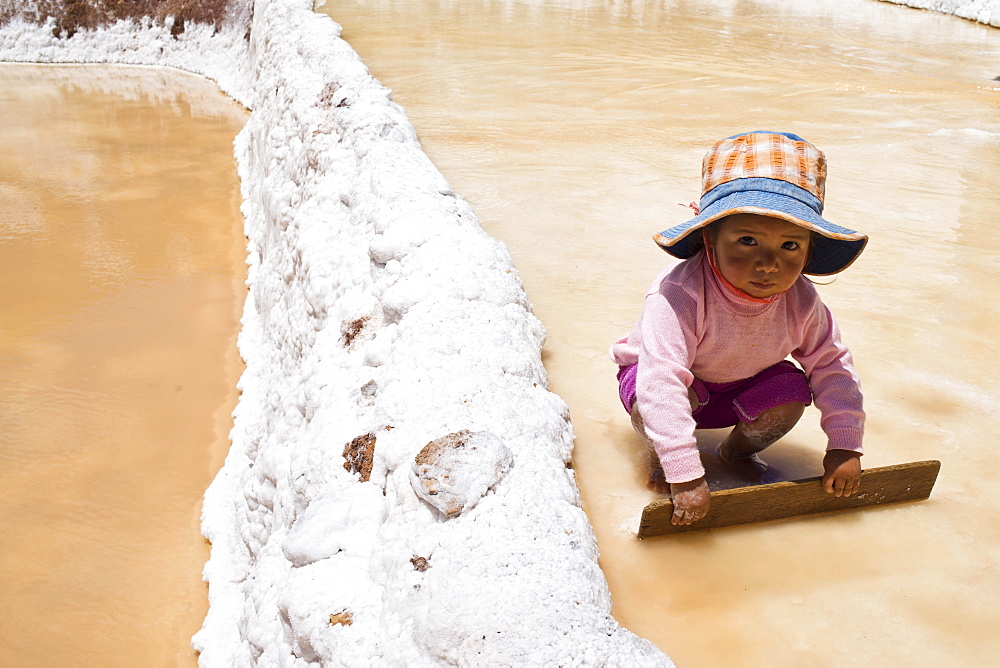 Child playing with a wooden board, Salinas de Maras salt pans, created by the Incas and still in operation, Pichingote, Cusco region, Andes, Peru, South America