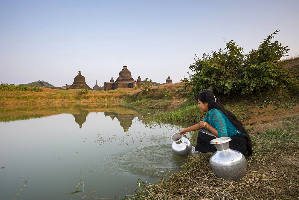 Smiling girl drawing water from a water hole with a vessel made of aluminium, Laymyetnta Pagoda or Temple, Mrauk U, Sittwe District, Rakhine State, Myanmar, Asia