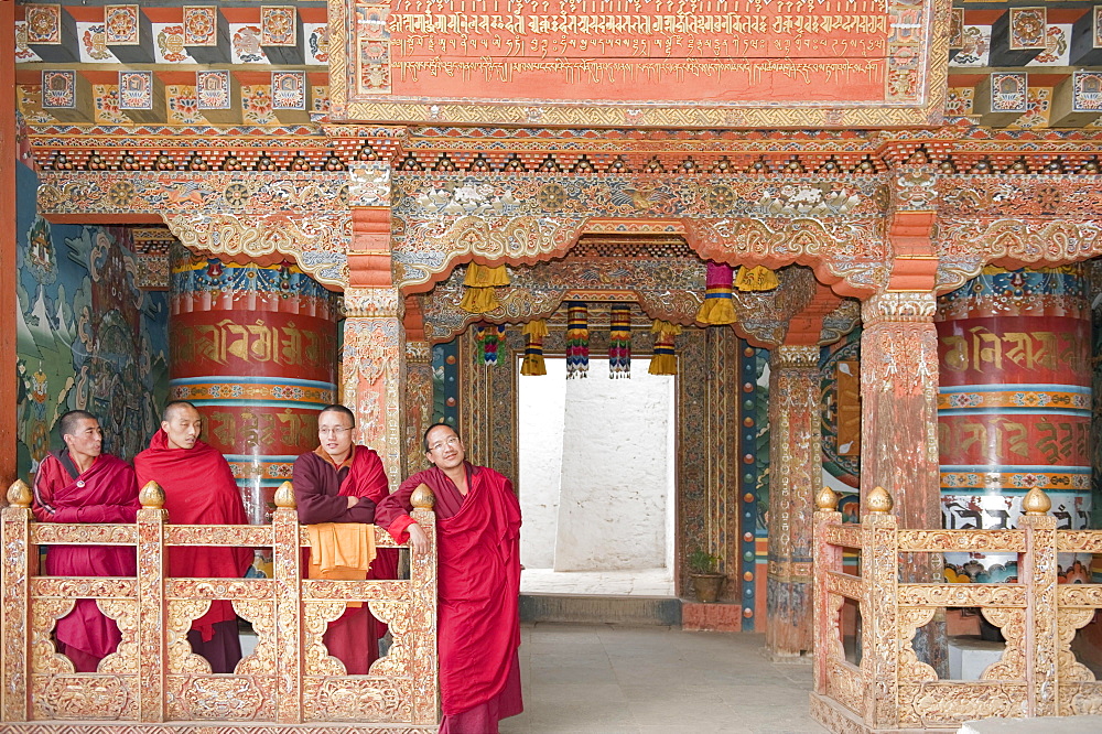 Four monks in red robes, ornate wooden wall, Buddhist Tango Goemba Monastery near Thimphu, Kingdom of Bhutan