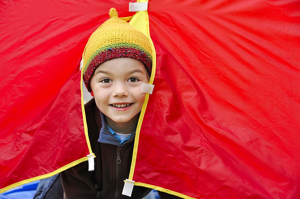 Boy with a knited cap looking out of a red tent, happy, Germany, Europe