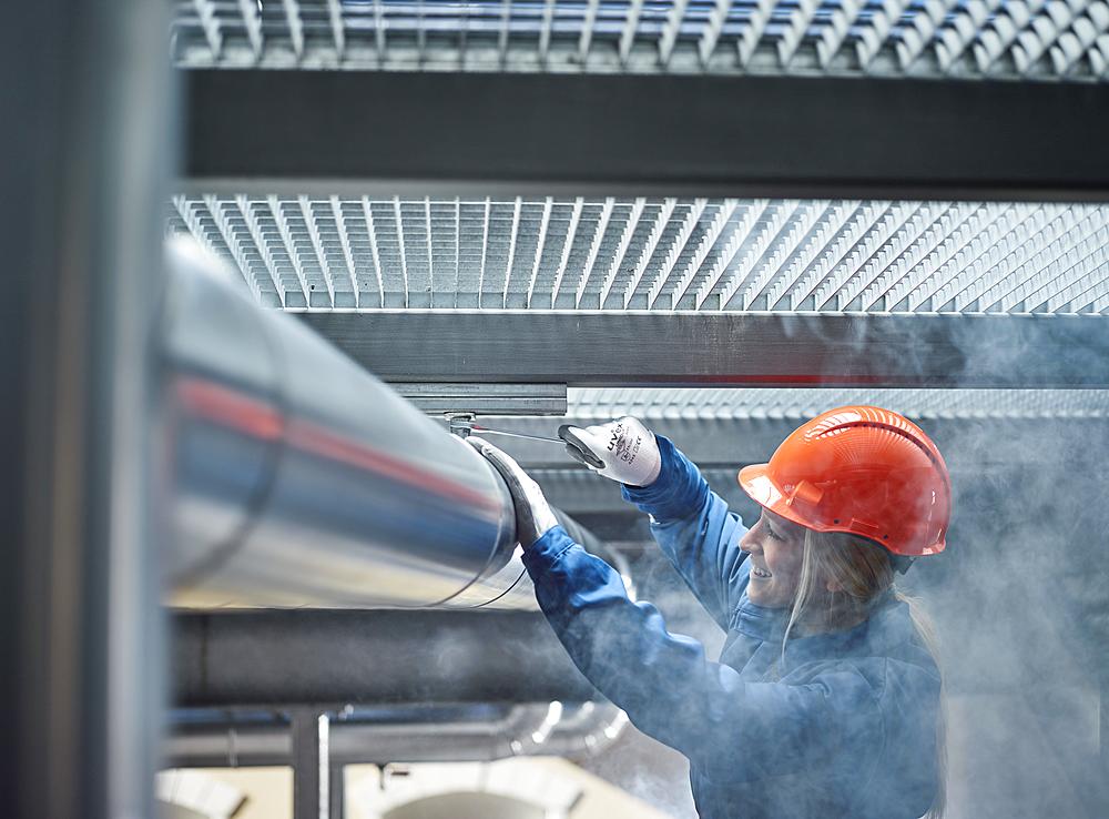 Technician, mechanic with orange helmet mounting a refrigeration line bracket, Austria, Europe