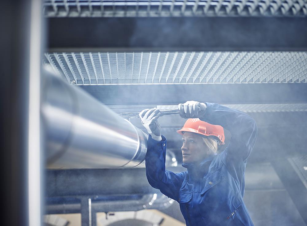 Technician, mechanic with orange helmet mounting a refrigeration line bracket, Austria, Europe