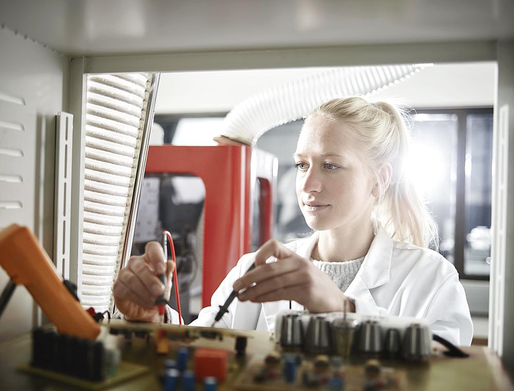 Young woman with white lab coat measuring controller with meter, Austria, Europe